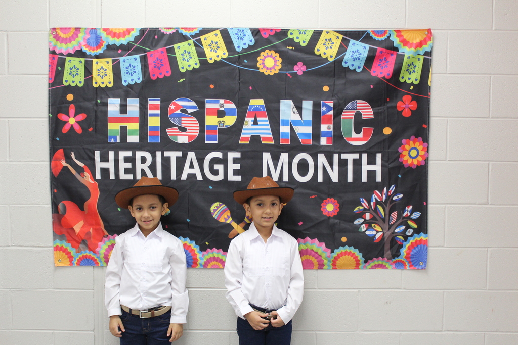Two students in traditional hispanic clothing in front of a sign that says Hispanic Heritage Month