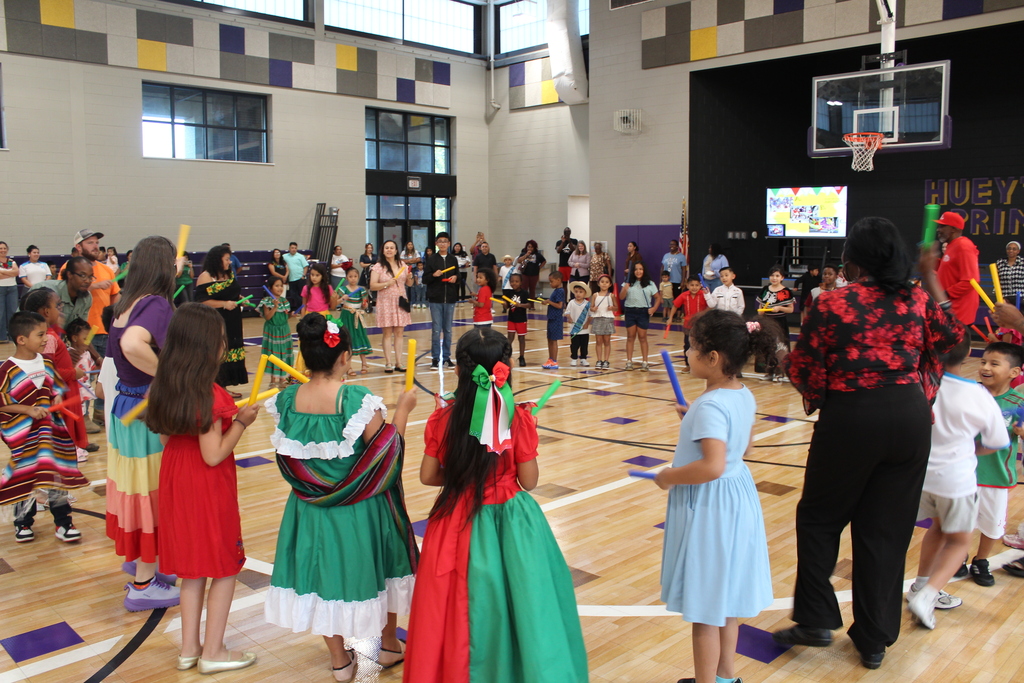 Students, teachers, and families in a circle in the gym holding rhythm sticks while dancing