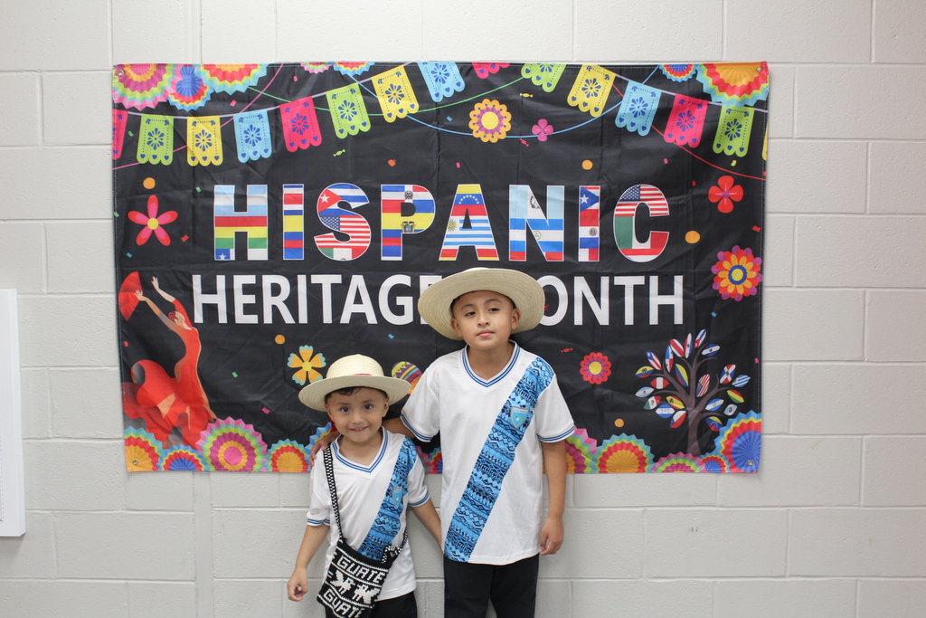 Two students in traditional hispanic clothing in front of a sign that says Hispanic Heritage Month