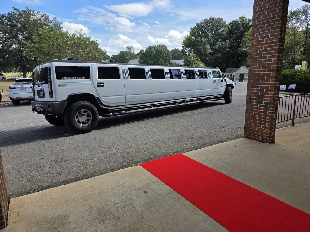 A white stretch, Hummer limousine parked outside of the school with a red carpet