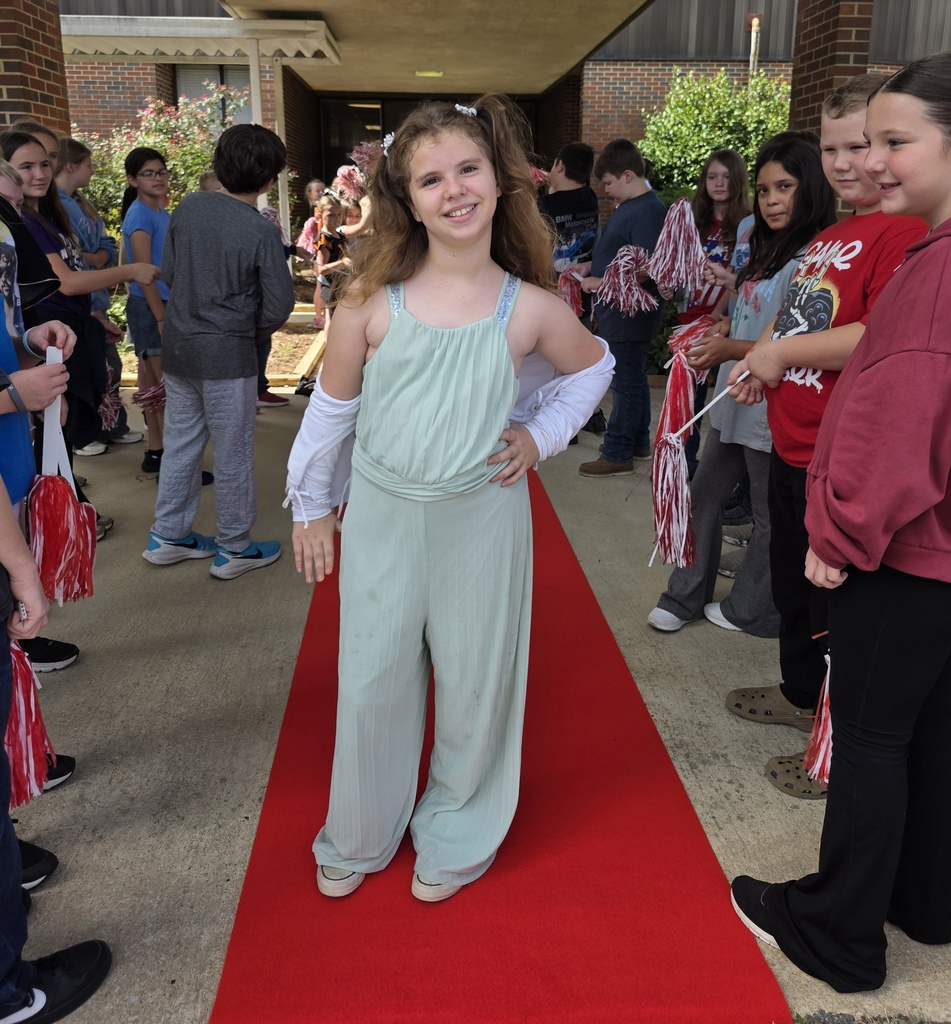 girl standing on red carpet with students shaking shakers around her