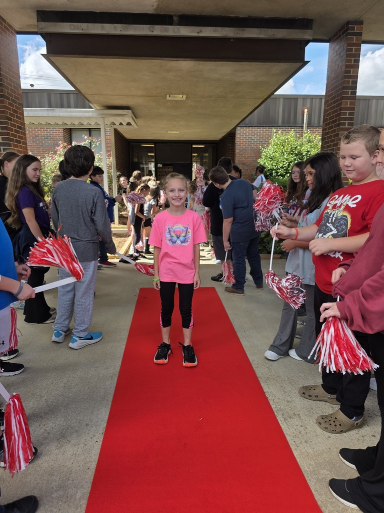 girl standing on red carpet with students shaking shakers around her