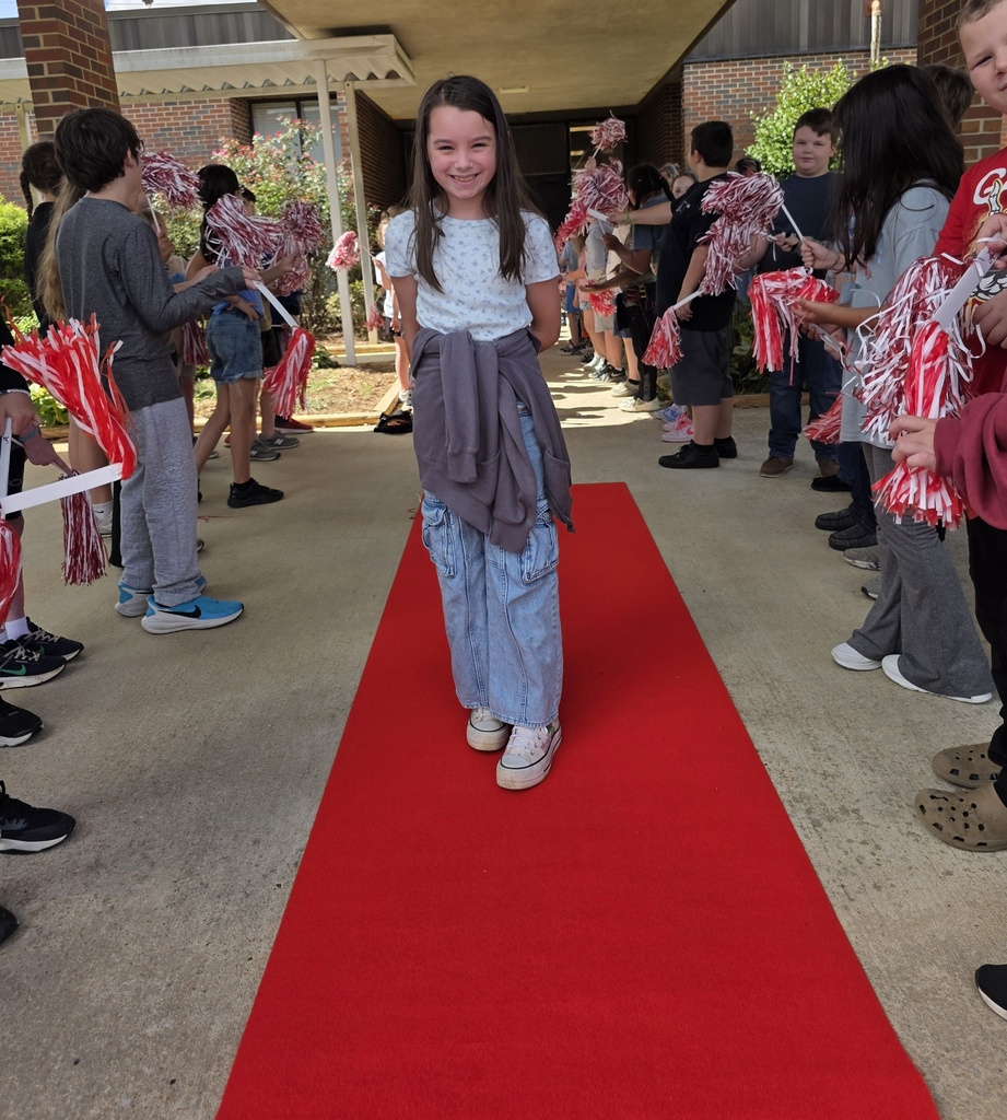 girl standing on red carpet with students shaking shakers around her