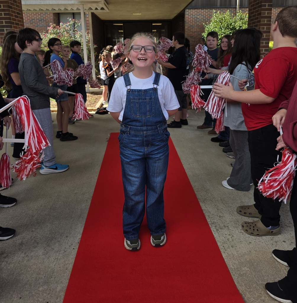 girl standing on a red carpet with students shaking shakers near him