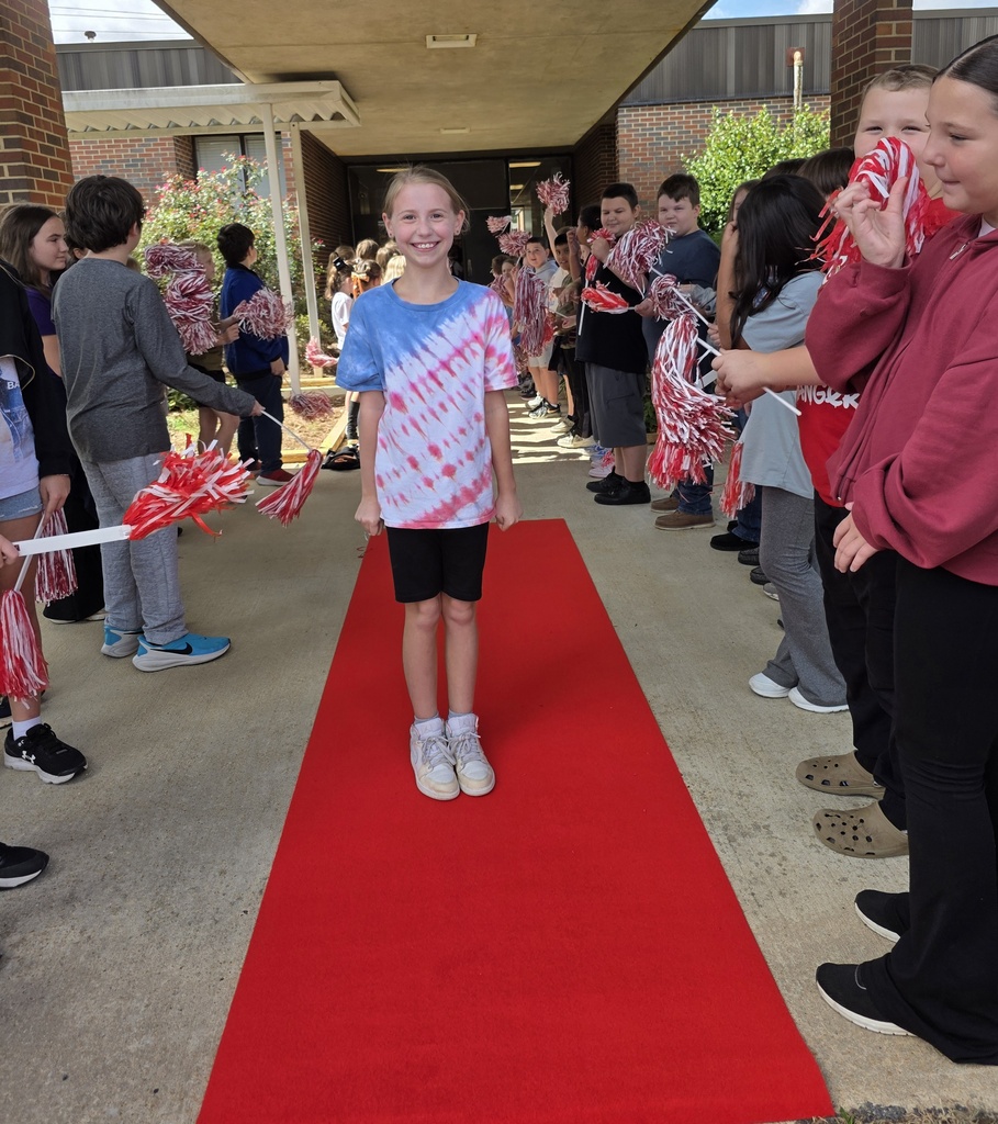 girl standing on a red carpet with students shaking shakers near him