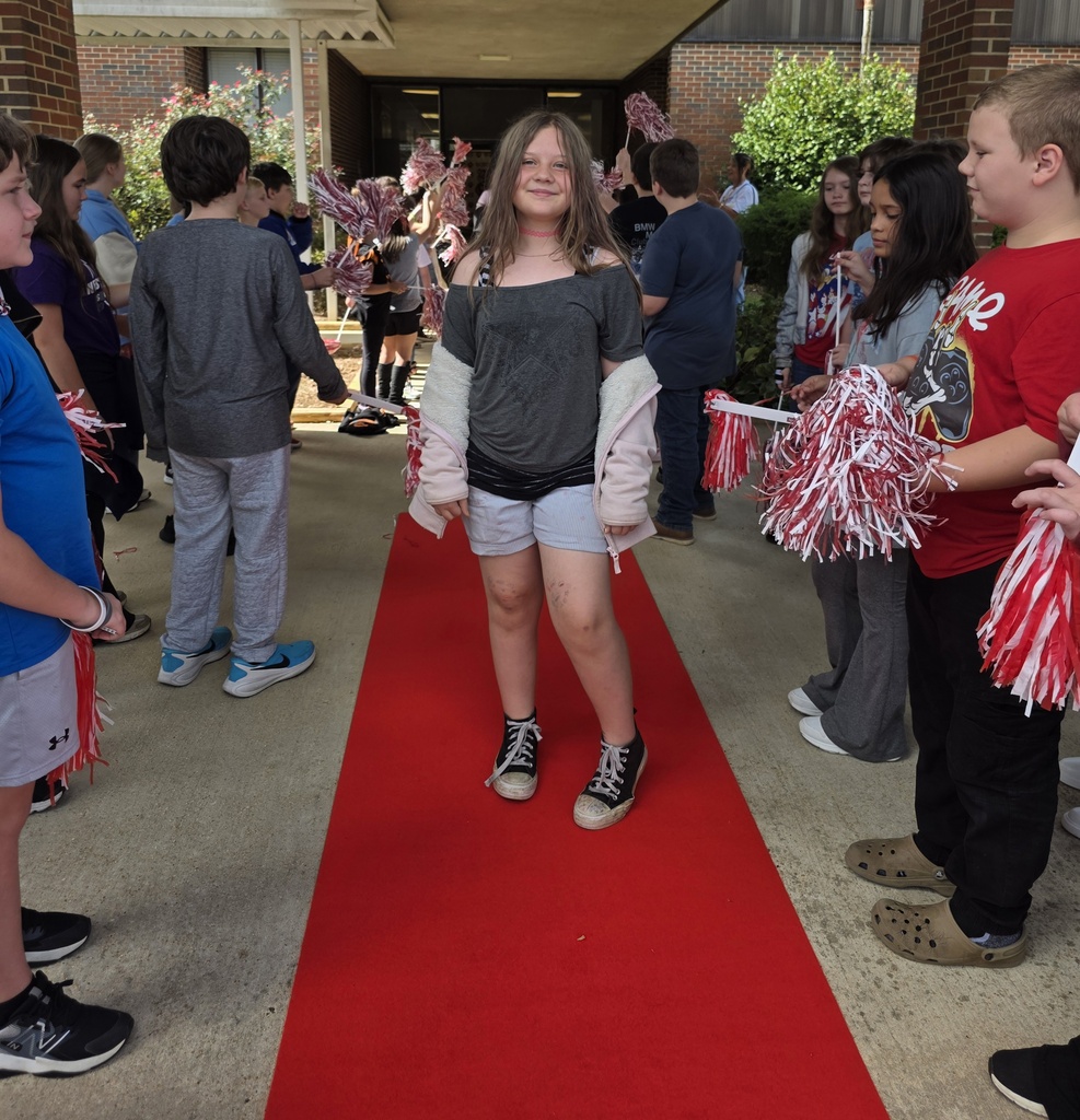 girl standing on a red carpet with students shaking shakers near him