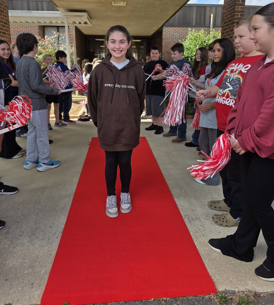 girl standing on a red carpet with students shaking shakers near him