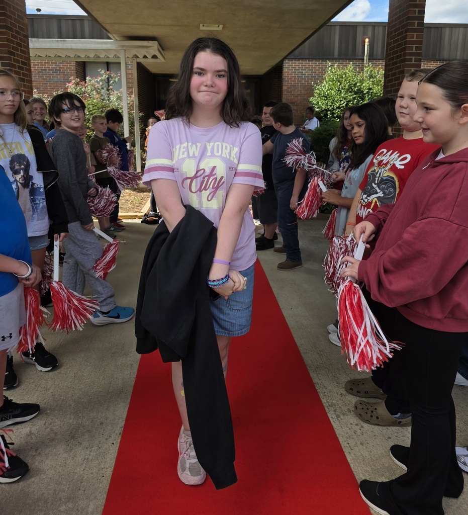 girl standing on a red carpet with students shaking shakers near him