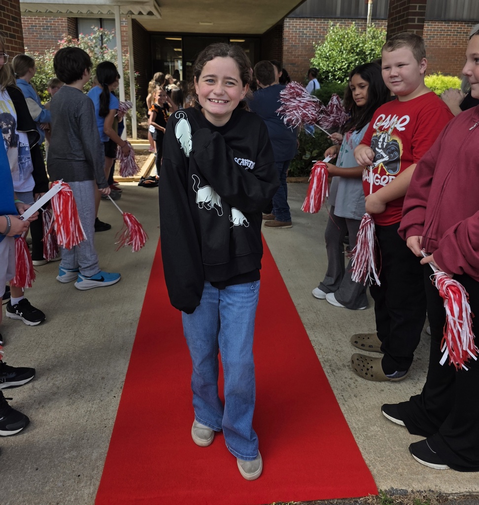 girl standing on a red carpet with students shaking shakers near him