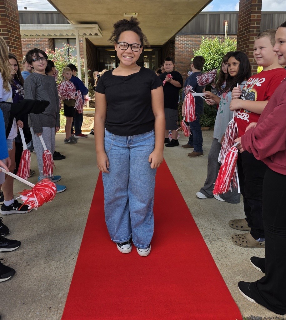 girl standing on a red carpet with students shaking shakers near him