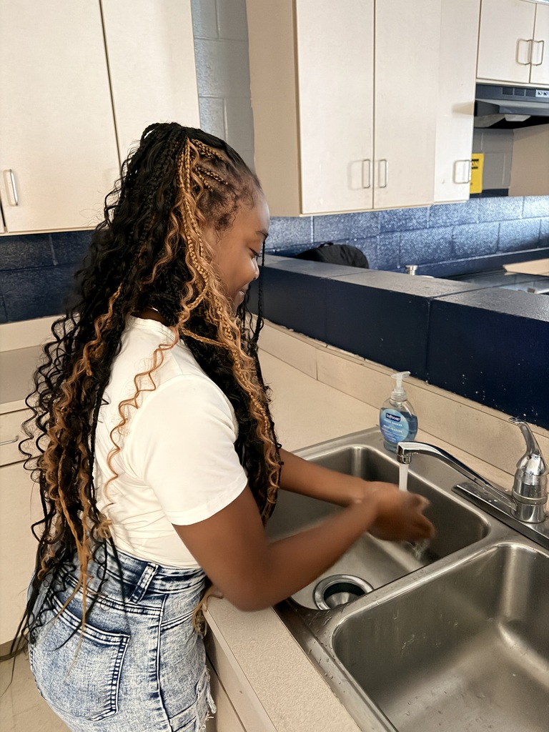Girl at the sink in a white tee and jeans washing her hands.
