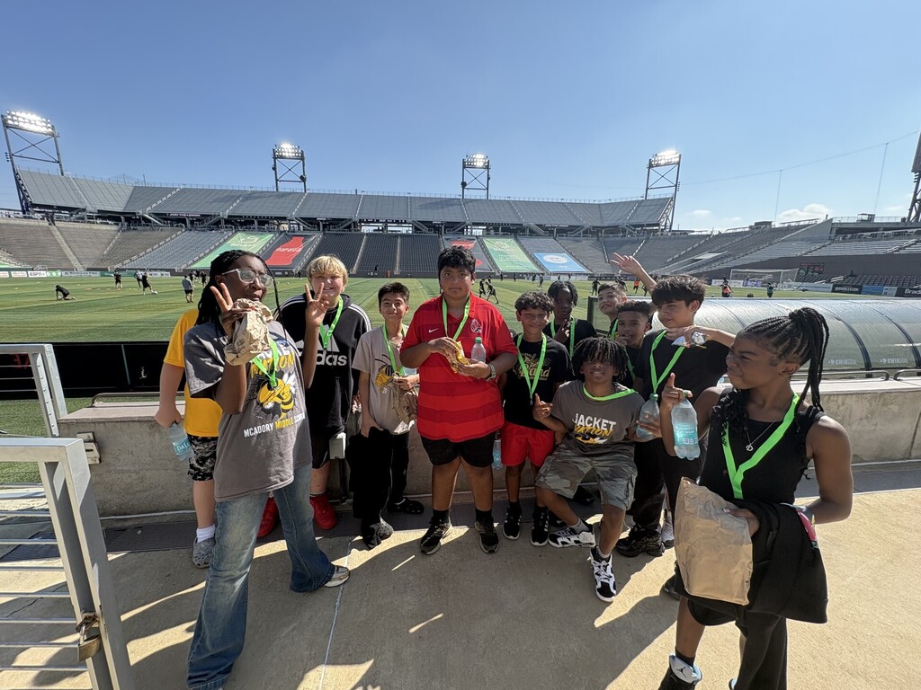 McAdory students posing at the railing with the soccer field and stadium seats behind them.