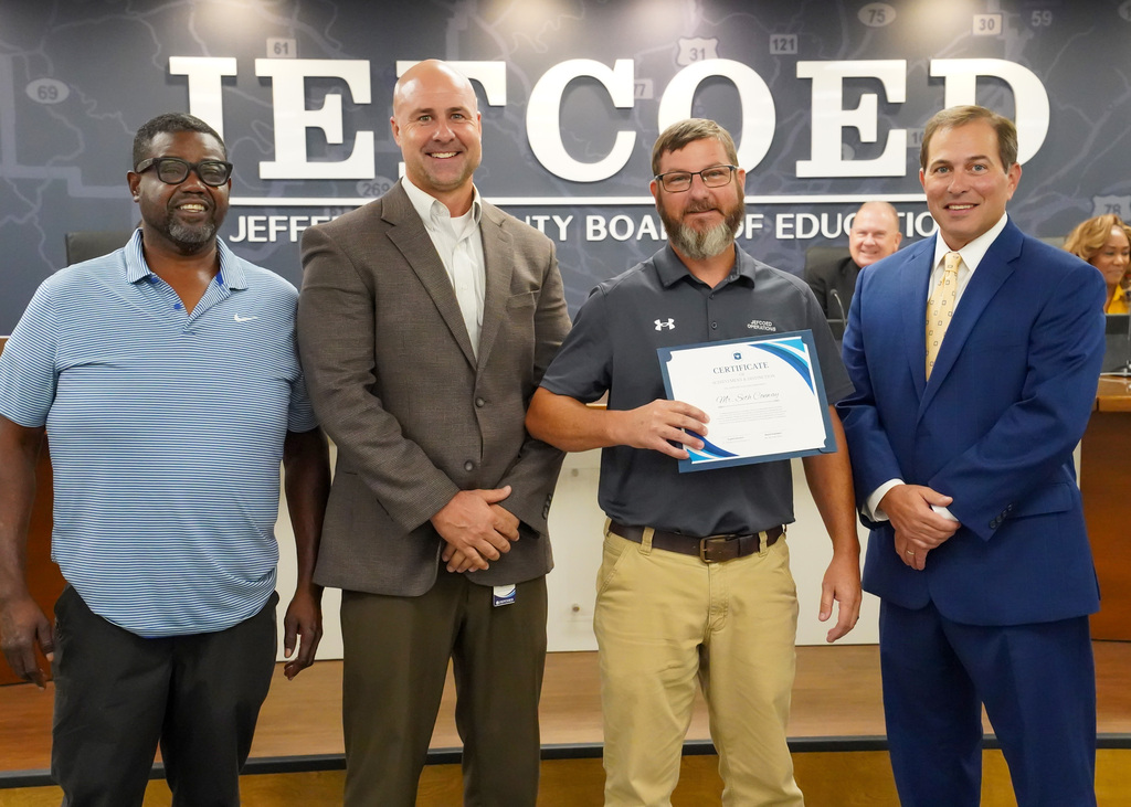 Mr. Seth Conway smiles for a photo with JEFCOED maintenance department officials inside the Jefferson County Schools board room.