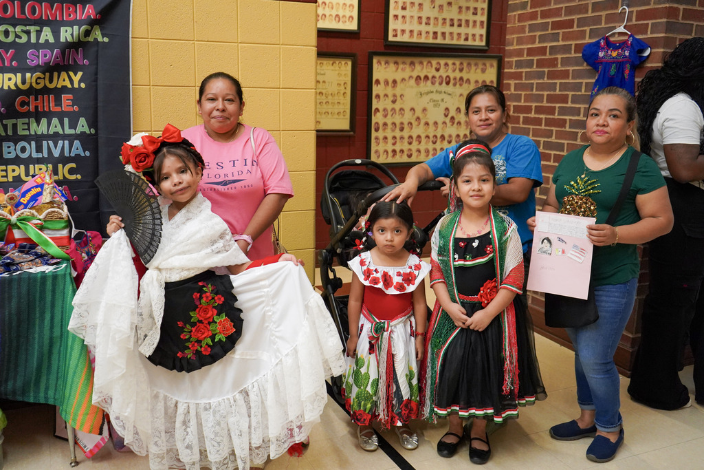 Women and children stand inside a school hallway and smile for a photo.