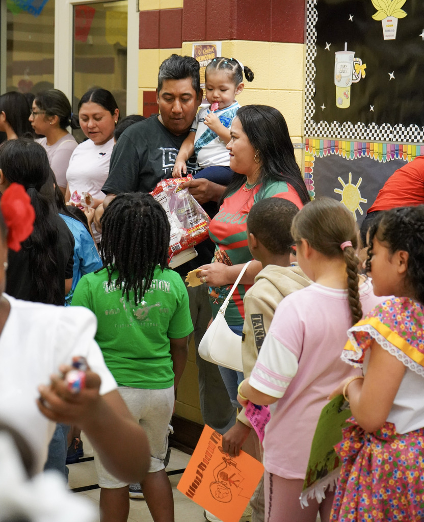 A family hands out candy to children in a school hallway.
