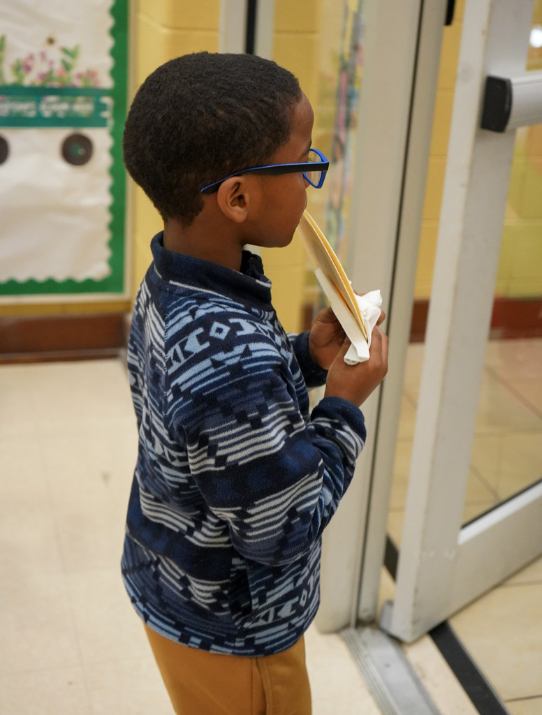 A child eats a tortilla while walking down a school hallway.