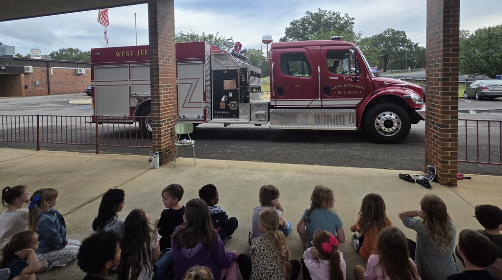 students sitting on the ground facing a firetruck