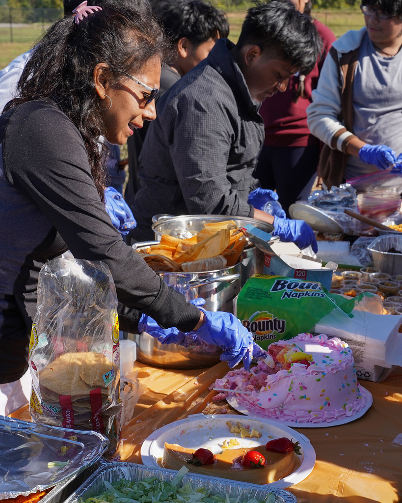 A woman cuts a piece of cake while serving at an outdoor Hispanic Heritage Month festival.
