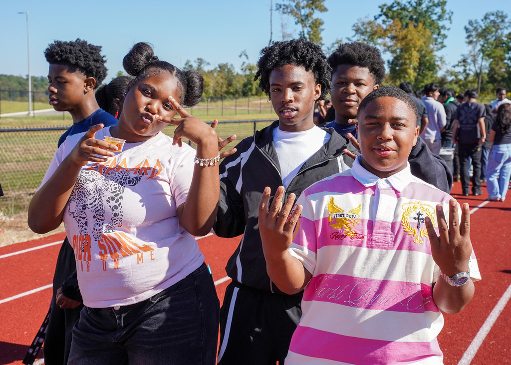 Students pose for a photo while standing on a track outside a school.