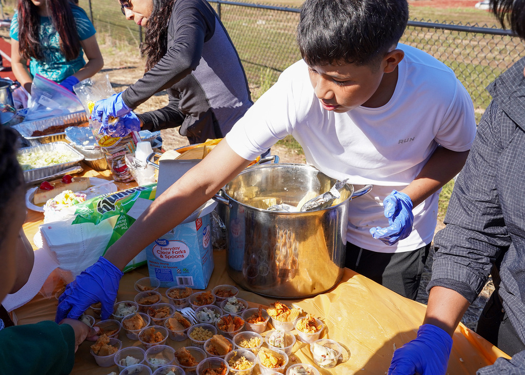 Students serve fellow students food from a table set up outdoors during a Hispanic Heritage Festival.
