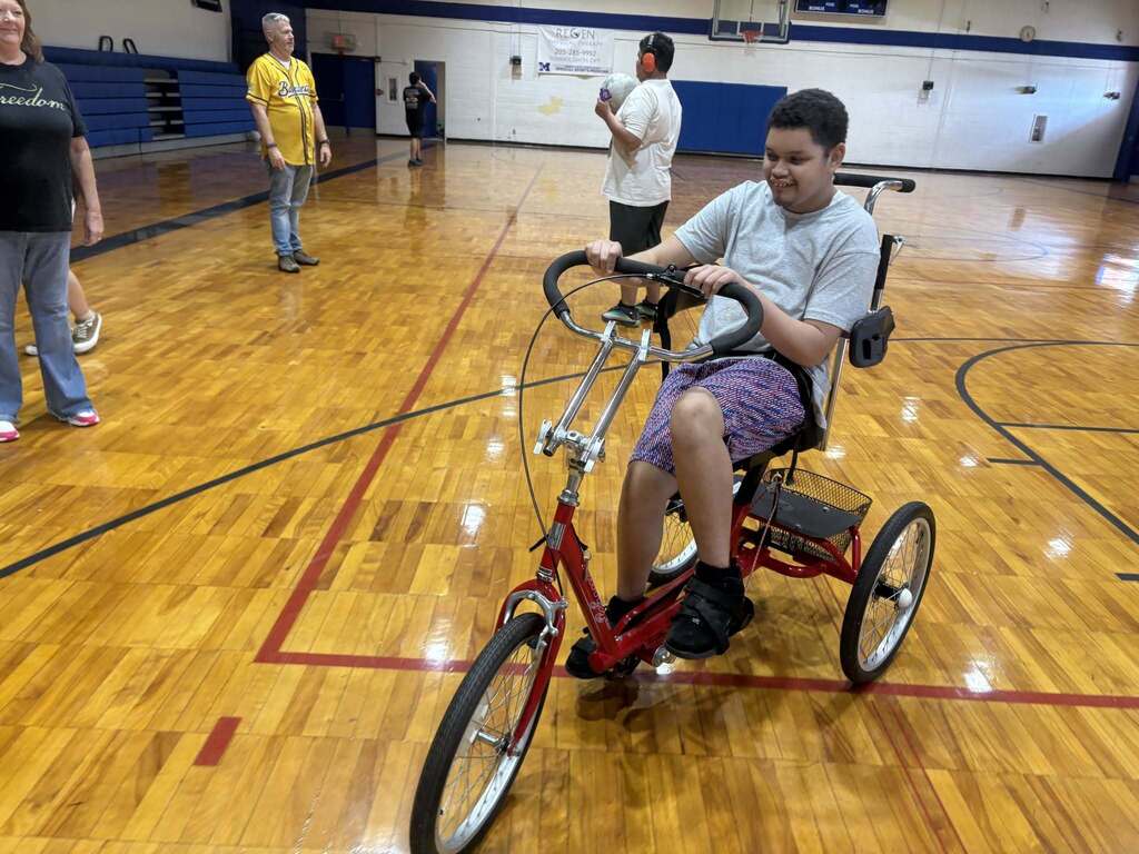A Burkett Center student rides an accessible tricycle through a school gym.