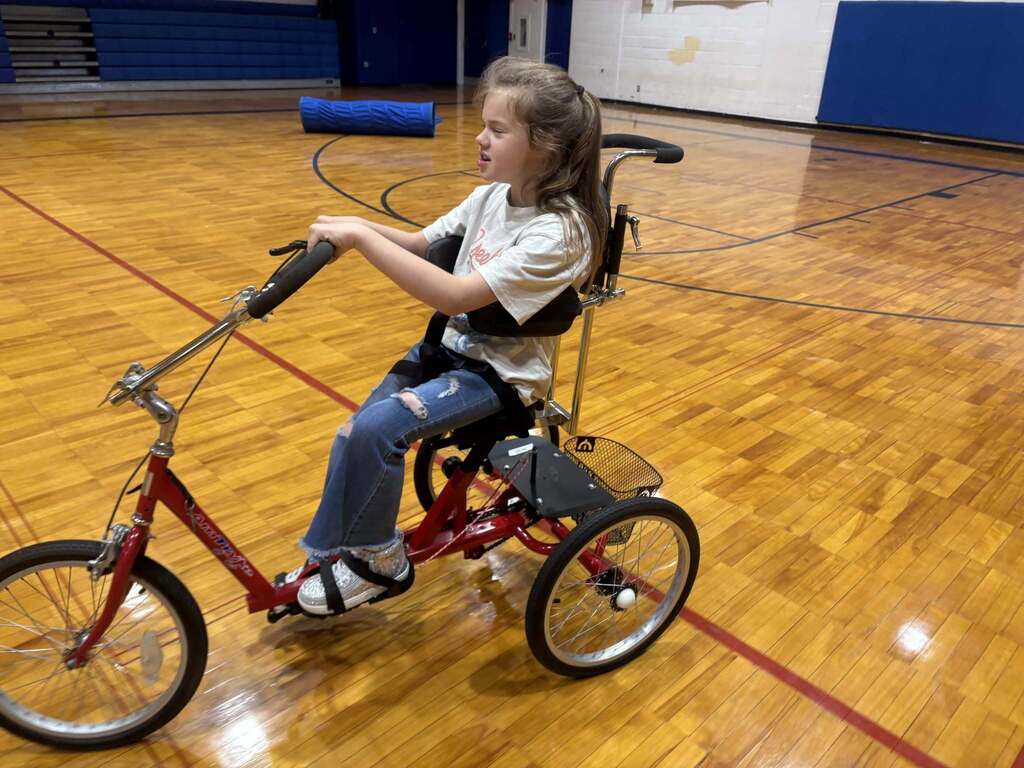 A Burkett Center student rides an accessible tricycle through a school gym.