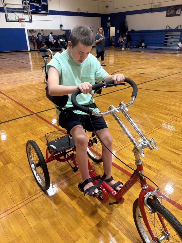 A Burkett Center student rides an accessible tricycle through a school gym.