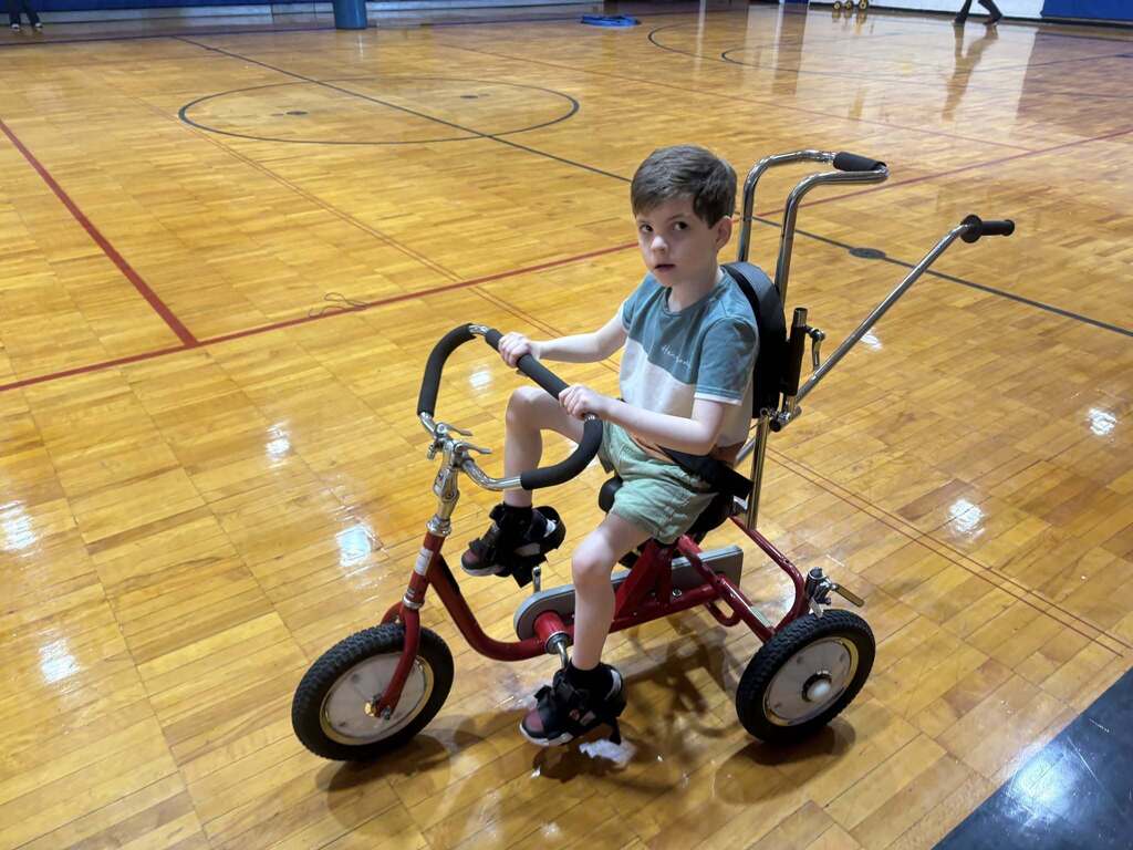 A Burkett Center student rides an accessible tricycle through a school gym.