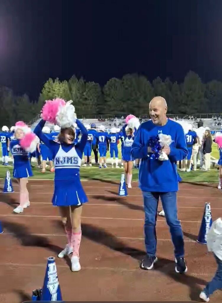 Mr. Henderson cheering with the cheerleaders on the sidelines of a football game