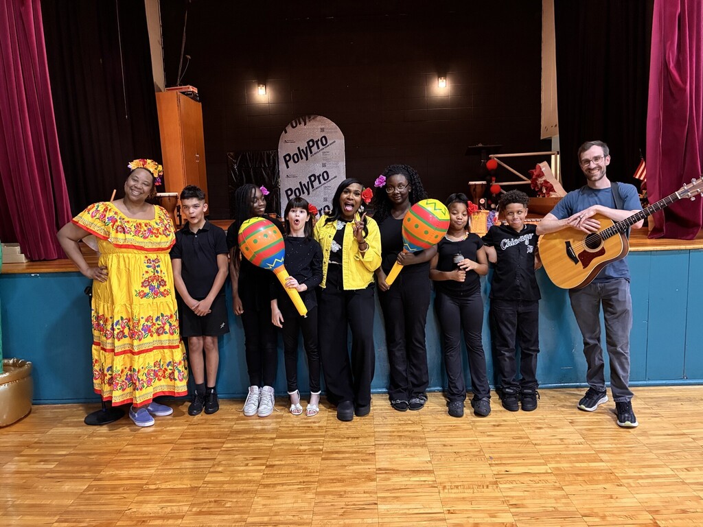 Ms. Bates and Ms. Crawford pictured with the choir students and the guitarist in front of the stage.