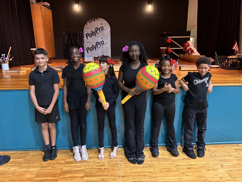 Choir students posing in front of the stage holding giant maracas. 