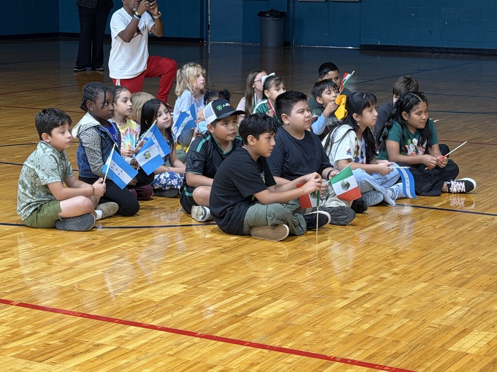 Students sitting on the gym floor with mini flags from different Hispanic countries.