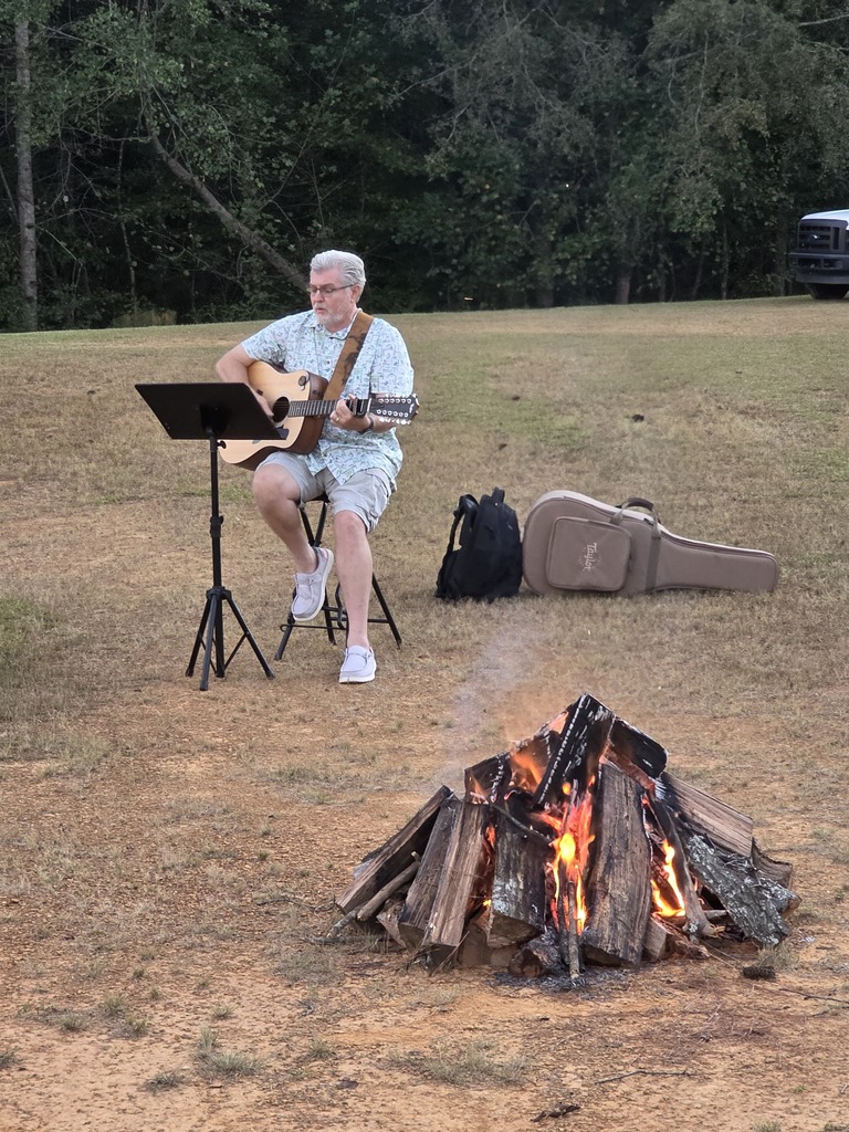 man playing guitar by a campfire