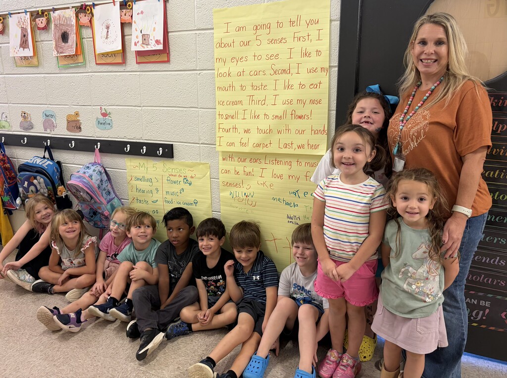 students sitting and standing in the hallway with teacher standing in front of classwork on the wall