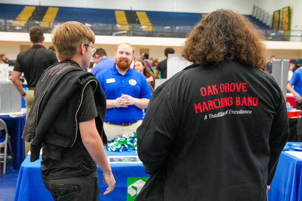 Students speak to a college recruiter during a college fair in a gymnasium.