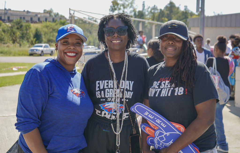 Three women stand together for a photo outside a baseball field.