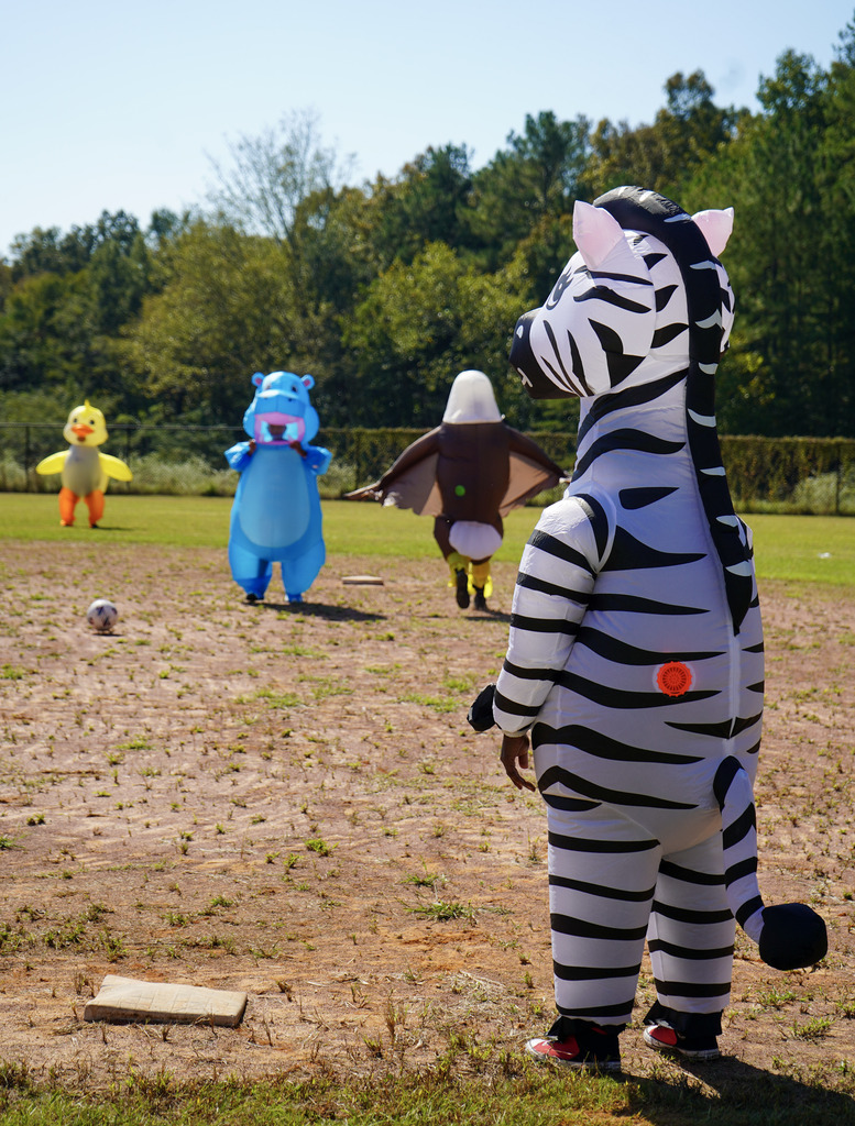 People wearing inflatable costumes play a game of kickball on a baseball field.