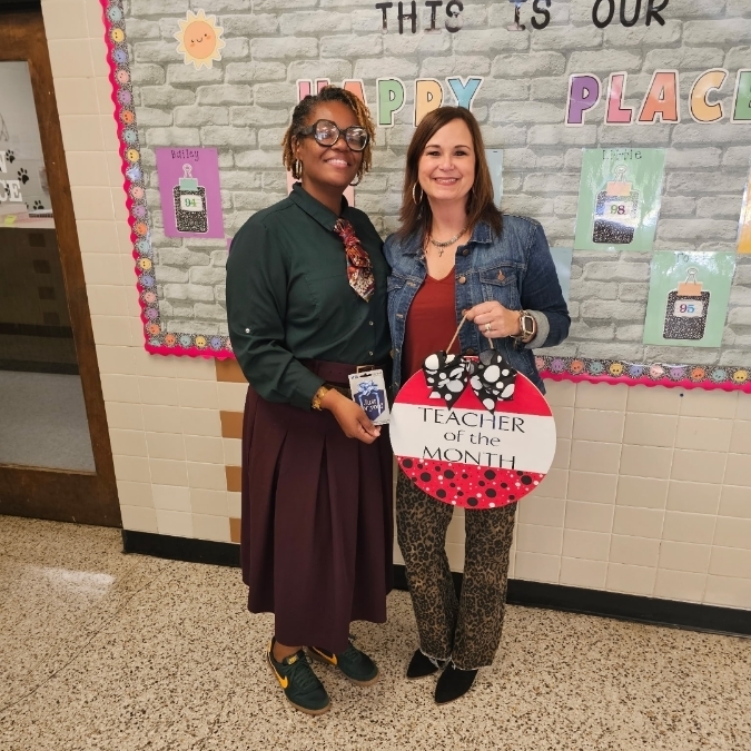 Principal Harris poses with Mrs. Motte, who is holding a teacher of the month door sign. 