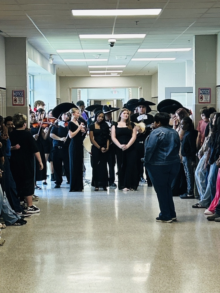 Pinson Valley High School mariachi performers play instruments in an HMS hallway while students watch.