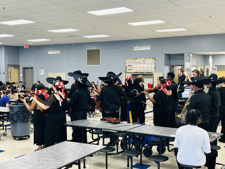 Mariachi musicians in black outfits and traditional hats perform for HMS students in the cafeteria.
