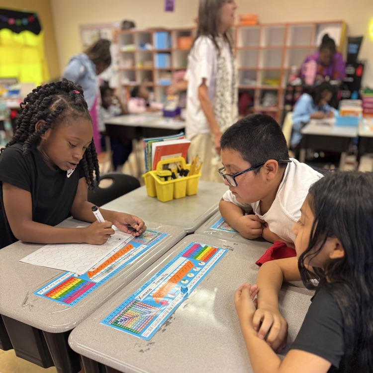 three students are working in a group as one writes on a paper