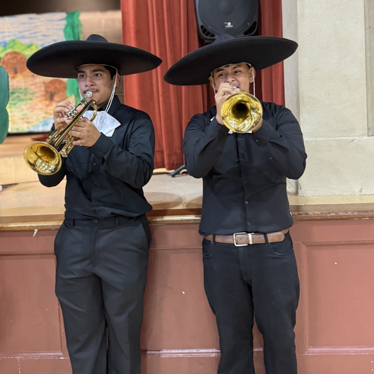 two mariachi band members blowing trumpets