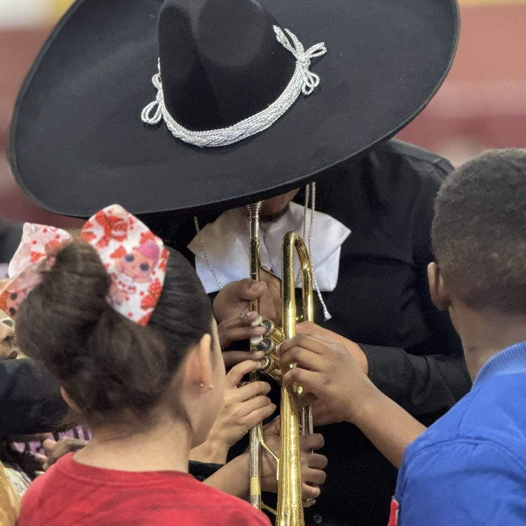 students touching a trumpet while a mariachi band member demonstrates how to play it
