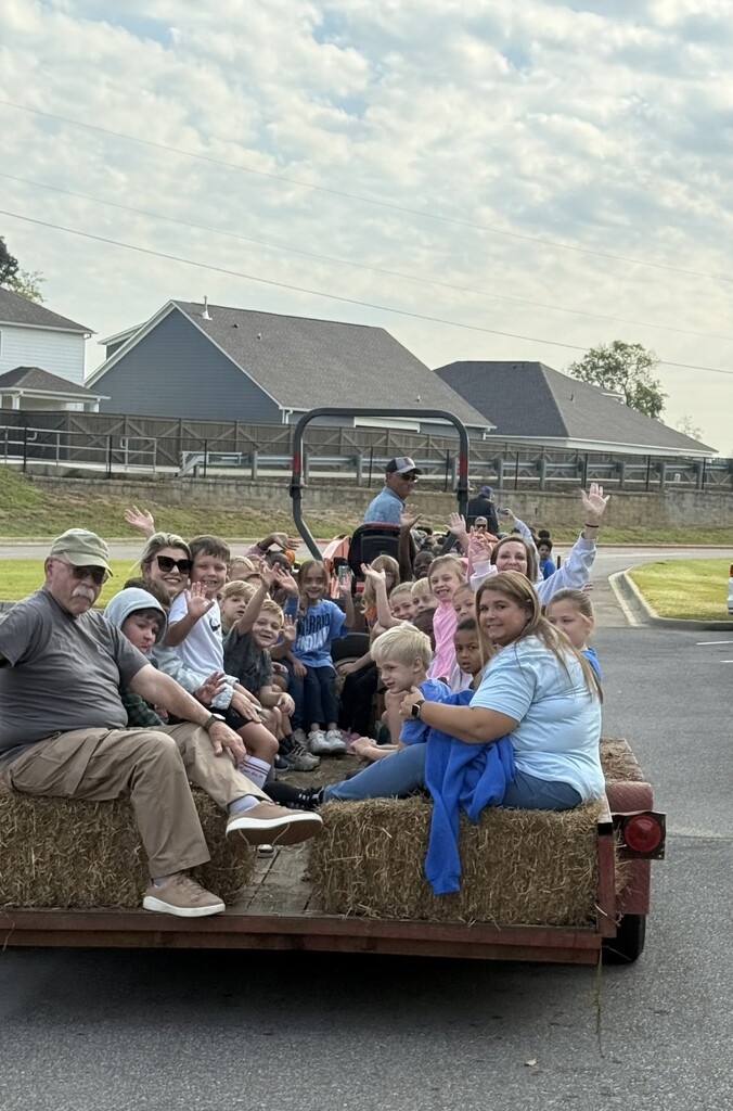 Teacher and students sitting on hay bales on the trailer getting ready to go on a hay ride 