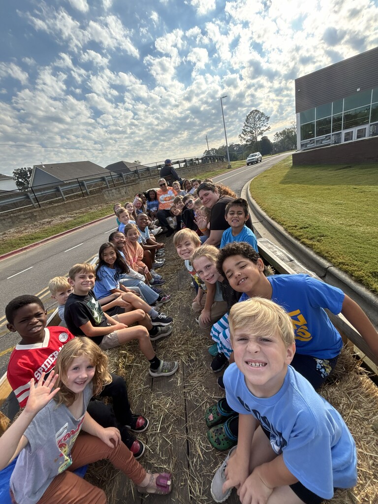 Teacher and students sitting on hay bales on the trailer getting ready to go on a hay ride 