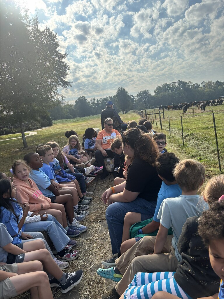 Teacher and students sitting on hay bales on the trailer getting ready to go on a hay ride 
