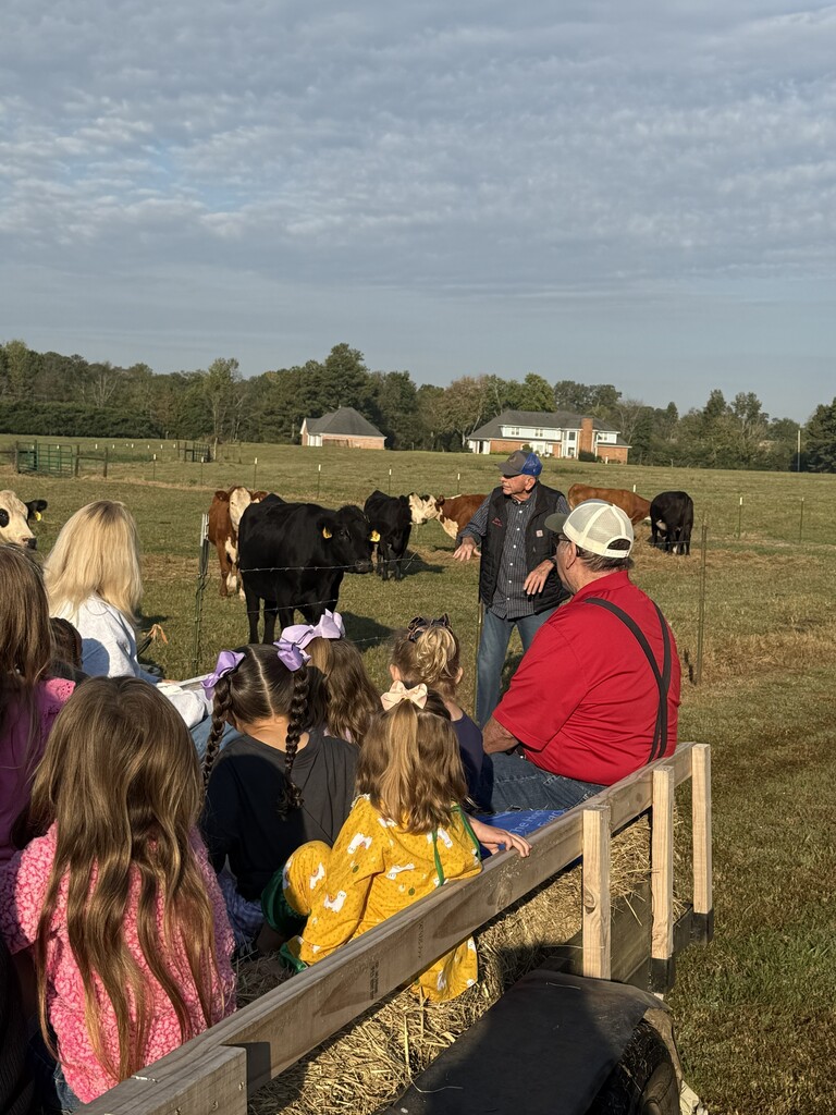 Mr. Baker is standing outside of the fence at the cow pasture and the stuents are on the trailer listening to him talk.