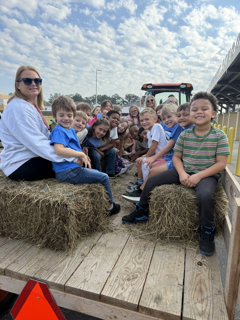 Teacher and students sitting on hay bales on the trailer getting ready to go on a hay ride 
