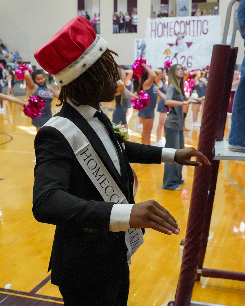 A student wearing a homecoming king crown and sash conducts a band.