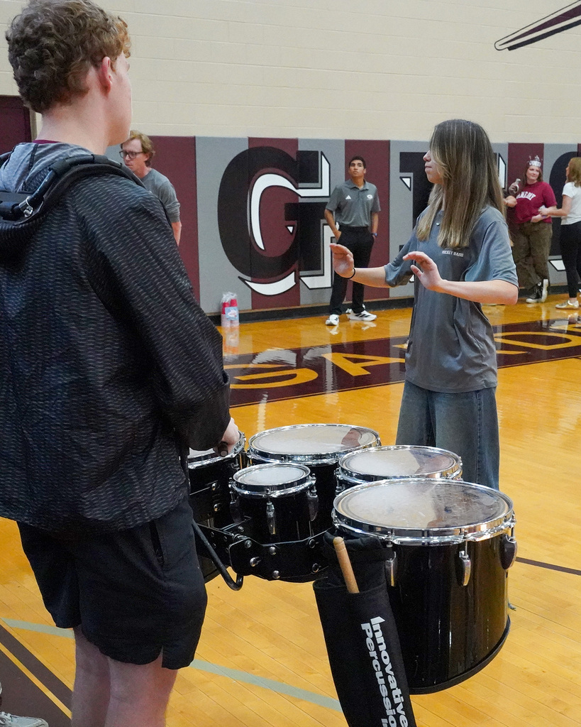 A student conducts band members as they play during a pep rally in a school gym.
